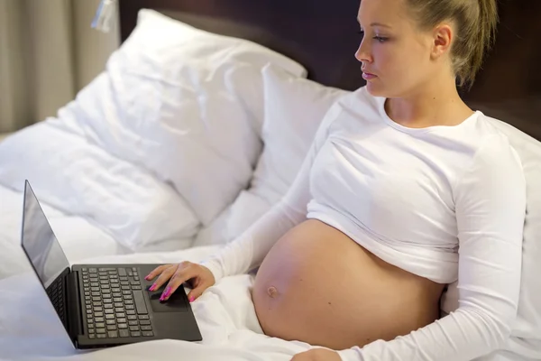 Femme enceinte dans son lit travaillant sur ordinateur — Photo