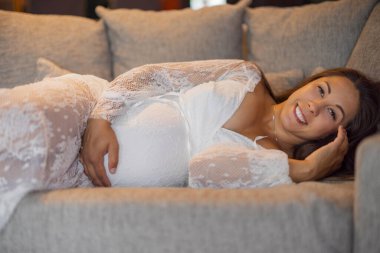 Bekleyen neşeli bir anne koltukta dinleniyor ve hamilelik yolculuğunu sıcak bir gülümsemeyle kucaklıyor. Narin bir dantel elbise giyince, sahne rahatlık, sevgi ve beklenti saçar..