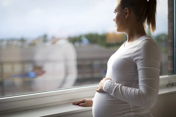 Femme enceinte réfléchie regardant par la fenêtre — Photo