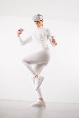 VR gözlük takan genç bir kadın beyaz arka planda dövüş sanatları yapıyor.