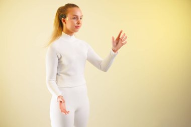 Akıllı gözlüklü genç bir kadın sarı arka planda dururken el kol hareketi yapıyor.