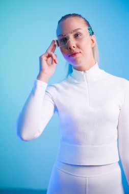 Mavi neon arka planda dururken akıllı gözlük kullanan kendinden emin bir kadın.