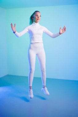 Akıllı gözlüklü genç bir kadın parlak mavi arka plana atlıyor.