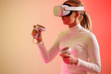 Elinde joystick tutan sanal gerçeklik gözlüğü takan bir kadın aydınlanmış neon renkli arka plana karşı.