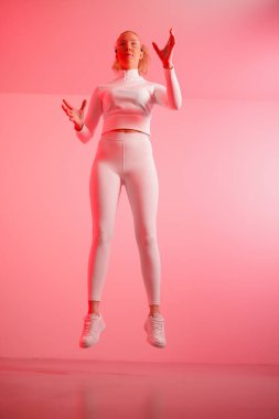 Akıllı gözlüklü genç bir kadın kırmızı arka planda el kol hareketi yapıyor.