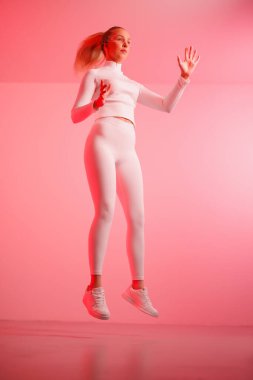 Kırmızı neon arka plana atlayan akıllı gözlüklü genç bir kadın.