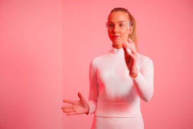 Kırmızı neon arka plana işaret eden akıllı gözlük takan kendinden emin genç bir kadın.