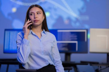 Bir güvenlik operasyonları merkezinde tespit edilmiş bir siber güvenlik analisti ekranlardaki gerçek zamanlı verileri izlerken, bu da proaktif olay tepkisini gösteriyor. Kadın bir telefon görüşmesinde işbirliği ve profesyonel ihtiyatı vurguluyor.