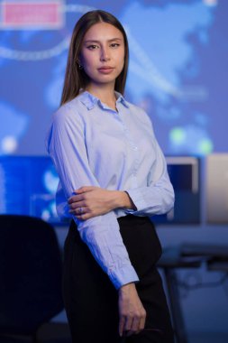 Teknoloji odaklı kontrol odasında kendine güvenen genç bir kadın profesyonelliği ve odaklanmayı kucaklıyor. Modern mavi temalı arka plana sahip sofistike bir ortam, teknolojik gelişim ve analitik düşünce duygusunu aktarıyor..