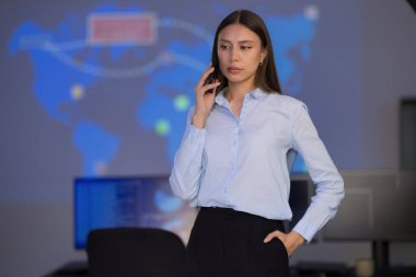 Güvenlik operasyonları merkezinde profesyonel bir kadın. Yüksek teknolojili bir iş yerindeki ekranlardaki tehdit verilerini analiz ediyor. Ayarlar küresel veri görsellerini içeriyor, dinamik bir çalışma ortamı sergiliyor. Sahne teknoloji güdümlü takım çalışmasını vurguluyor