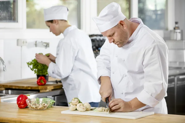 Dois chefs profissionais preparando legumes em grande cozinha — Fotografia de Stock