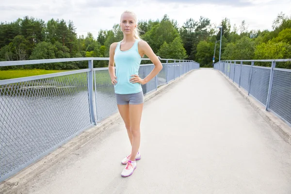 Beautiful and confident young female runner stands at bridge — Stock Photo, Image