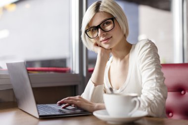 Gülümseyen genç kadın kafede dizüstü bilgisayar ile çalışma