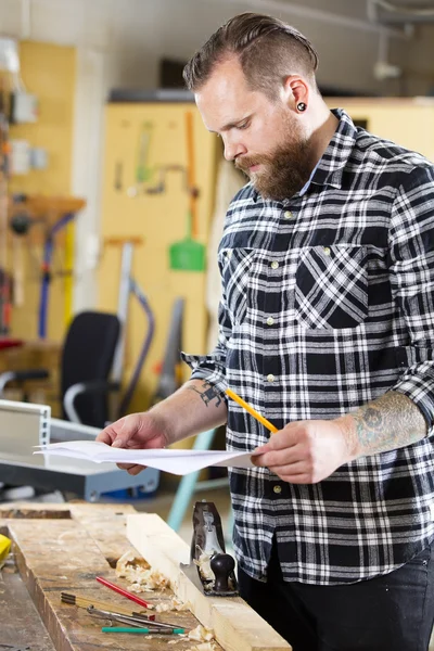 Timmerman planning van werkzaamheden en kijken naar tekeningen in de werkplaats — Stockfoto