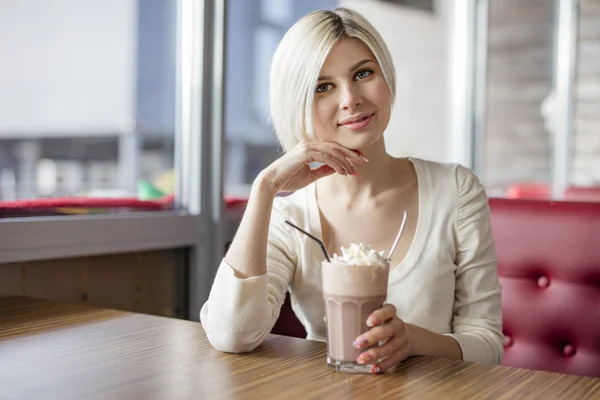 Smiling young woman drinking hot chocolate with cream at cafe — Stock Photo, Image