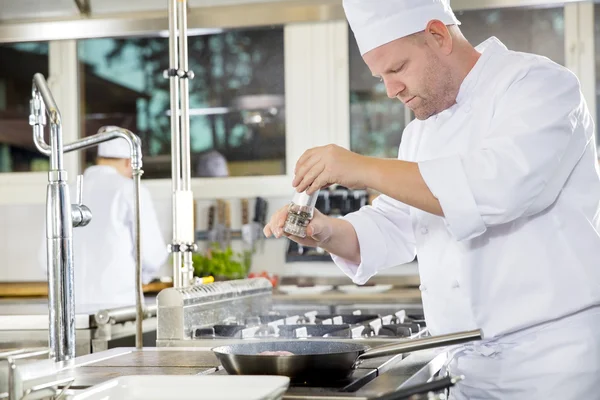 Chef ajoutant du poivre sur le steak dans une cuisine professionnelle — Photo