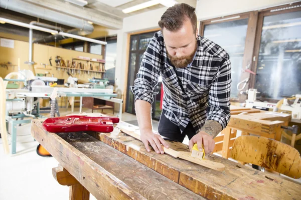 Carpintero lijando un cuello de guitarra de madera en taller — Foto de Stock