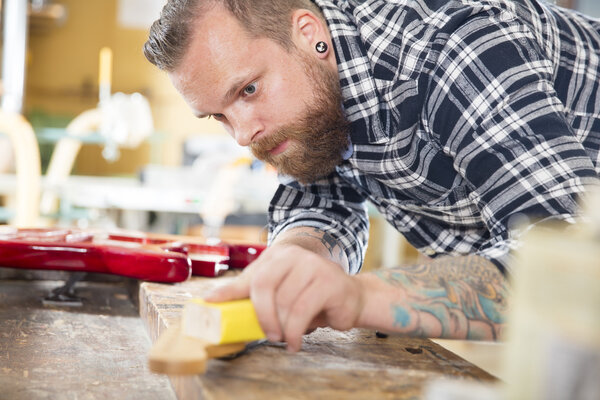 Carpenter sanding a guitar neck in wood at workshop