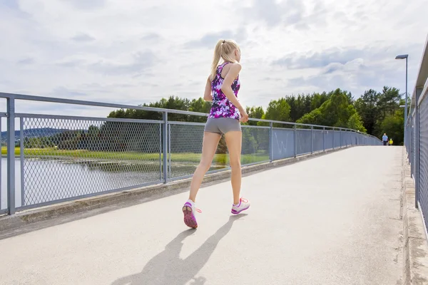 Schlanke Frau läuft auf Brücke über See ins Freie — Stockfoto