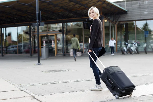Улыбающаяся молодая женщина, путешествующая с чемоданом на колесах — стоковое фото