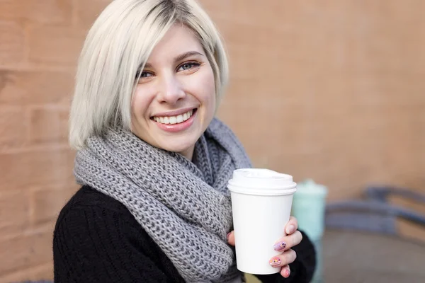 Улыбающаяся блондинка пьет кофе на открытом воздухе в кафе — стоковое фото