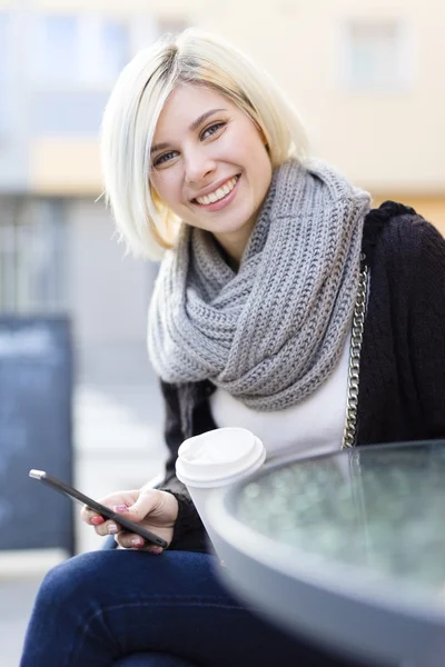 Usmívající se žena s kávou a pomocí telefonu venkovní — Stock fotografie