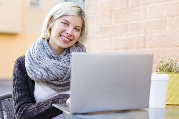 Mujer sonriente trabajando con el ordenador portátil al aire libre en la cafetería — Foto de Stock
