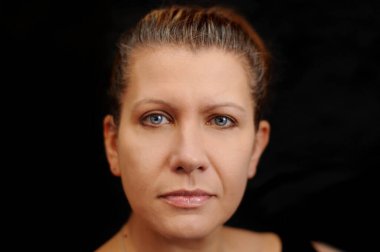 Siyah arka planda kızgın bir yüzü olan orta yaşlı bir kadın. Gri saç boyamaya vakit bulamadığı için üzgün.