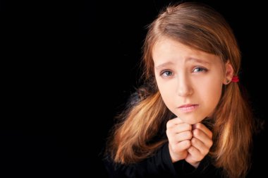 Portrait of a young girl on a black background. She is prayerfully prayed. She asks God for help. Horizontal. Copy space clipart