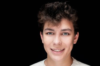 Siyah arka planda beyaz gömlekli bir adamın portresi. Dişlerindeki diş telleri açıkça görülüyor. Gülümsüyor. Yatay olarak. Metin için yer