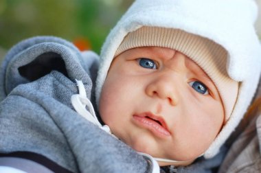 Küçük bir çocuk, sıcak kıyafetler içinde ve ilkbaharda yürüyüşe çıkmış sıcak bir şapka takıyor. Ciddi bir yüzü ve güzel mavi gözleri var.