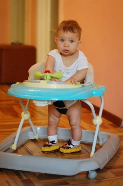 Küçük bir çocuk evde bebek yürüyenlerin içinde oturuyor. Dikey
