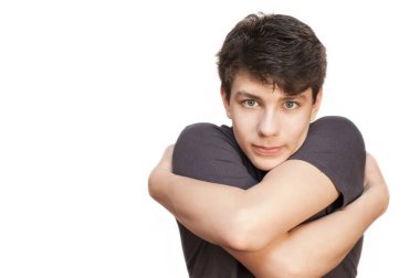 Genç çocuk beyaz bir arka planda kendine sarılıyor. İzole edilmiş. Ciddi ama çok güzel bir yüzü var. Ailesi ve akrabaları tarafından sarılmaya ihtiyacı var.