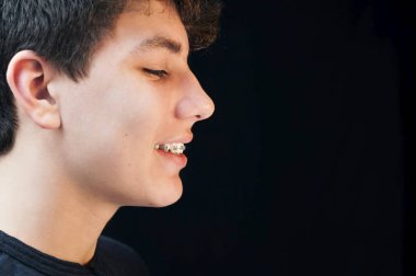 Siyah arka planda profili olan bir adamın portresi. Onun gülümseyen hoş bir yüzü var. Diş telleri dişlerine takılı. Diş Konsepti