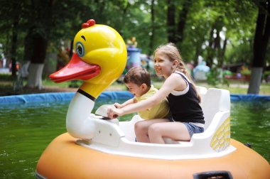 Çeşitli çocuklar - küçük bir oğlan ve genç bir kız parkta büyük bir ördek şeklinde suyun üstünde yüzüyorlar. Bir abla küçük erkek kardeşiyle vakit geçirmeyi sever.