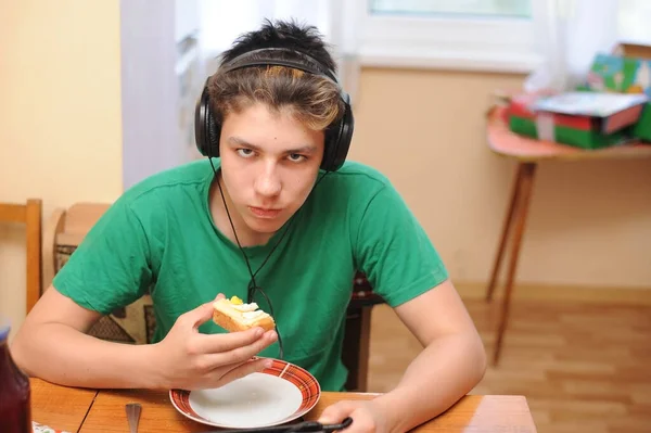 Adolescente Escucha Música Los Auriculares Sienta Cocina Come Sándwich Tiene —  Fotos de Stock