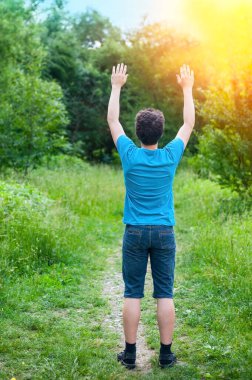 Bir genç parkta ellerini havaya kaldırmış ve dua ediyor. Tanrıyla vakit geçirmeyi seviyor, özellikle de doğada. Arka görünüm