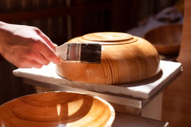 Delikanlının yeni bir hobisi var. Tabakları tahtadan oyup cilalıyor ve ailesine ve arkadaşlarına veriyor. Adam ahşap tabakları fırçayla cilalıyor. Seçici odak