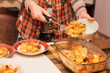 Evde bir kadın lezzetli bir akşam yemeği pişirdi. Sebzeli ve sosisli fırında patates ve tüm aile için tabağa yemek koyan bir kadın. Yatay
