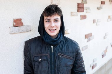 Başında başlığı olan, kışları duvarda duran ve gülümseyen sıcak ceketli genç bir çocuk. Adamın dişlerinde diş telleri olan güzel bir gülümsemesi var. Diş Konsepti