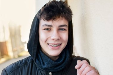 Yakışıklı genç bir çocuk yürüyüş sırasında gülümser ve şehirde dinlenir. Başında bir başlıkla sıcacık giyinmiş, dişlerinde diş telleri olan bir çocuk. Diş Konsepti