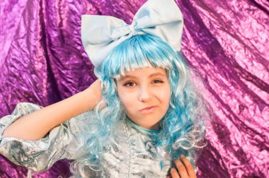 Mavi karnaval kostümlü pembe arka planda genç bir kız. Kızın komik bir yüzü var. Tiyatro sahnesinde oynamak için eğitilmiş.