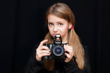 Sevimli genç bir kız elinde siyah arka planda profesyonel bir kamera tutuyor ve fotoğraf çekmeyi öğreniyor. Kız bir fotoğrafçının kariyerini hayal eder.