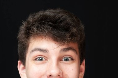 Karanlık bir arka planda, büyük gözleri, sevinç ve şaşkınlık duyguları olan mutlu bir gencin yarım yüzü, mesaj ve reklam için uygun bir yerde, bir adam bir şeyin reklamını yapmaktan mutluluk duyar.