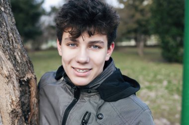 Genç bir adam kışın başında temiz havada koştuktan sonra vahşi doğada dinlenirken gülümser. Çocuğun dişlerinde diş telleri açıkça görülüyor. Diş Konsepti