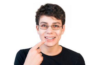 Gözlüklü bir çocuk arka planda gözlerini düzelttiği için ve dişlerindeki diş tellerinde parmağını gösterdiği için. Diş konsepti. Boşluğu kopyala