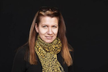 Orta yaşlı bir kadın koyu bir arka planda güzel bir şekilde gülümserken kuaföre gitti ve kuaför saçını gri olmasın diye çizdi. Kadın şimdi daha genç göründüğü için mutlu.