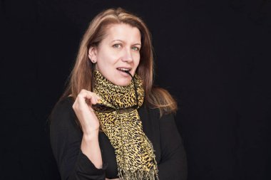 Boynunda leopar desenli bir eşarp olan güzel bir kadın karanlık bir arkaplanda güneş gözlüğü ve gülümseme tutuyor. Kadının çok güzel saçları var, onu beyaza boyuyor ki saçı görünmesin.