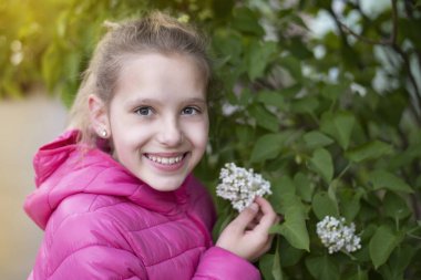 Genç kız leylak çiçeklerini zevkle kokluyor ve tüm samimiyetiyle gülümsüyor çünkü her şey çiçek açtığında ve kokladığında baharı seviyor.