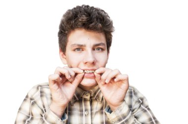 Korkmuş yüzlü bir çocuk sert kurabiyeler yerken dişlerine taktığı diş tellerini takmaya çalışır. İzole edilmiş. Bir çocuk diş tellerini kollarında tutuyor. Diş hekimi ve ortodontist konsepti